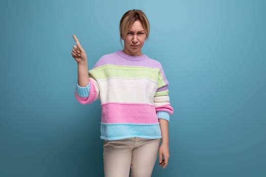 neat cute blond woman in a casual look shows her hands at the wall with copy space on a blue background.