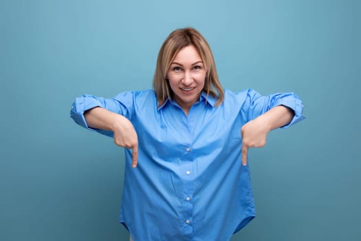 european blond young woman in casual shirt shows hands down at baner on blue background with copy space.