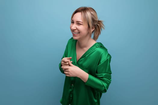 attractive blond young woman in green silk shirt laughing on blue background.