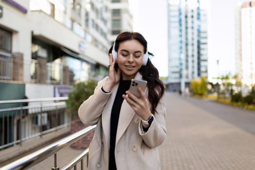 a woman listens to music on the street in headphones and looks at a mobile phone.