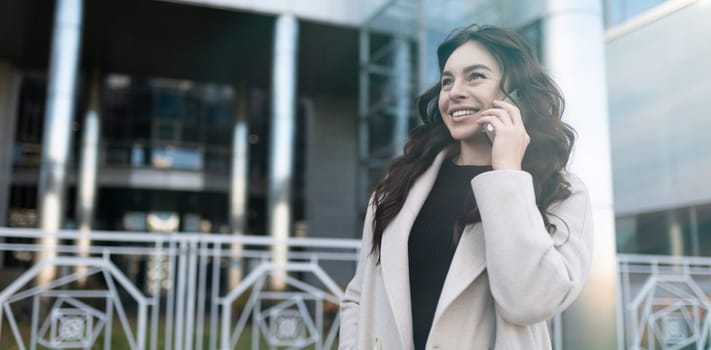 confident young businesswoman talking on mobile phone with a big smile on her face outside the office.