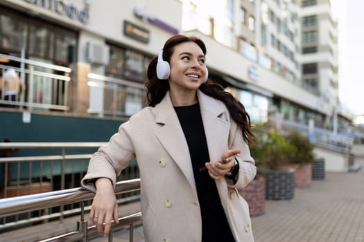 young stylish woman listening to music on headphones with a big smile on her face outside the office.