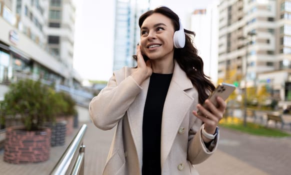 happy young woman in business clothes listening to music with headphones on mobile phone.