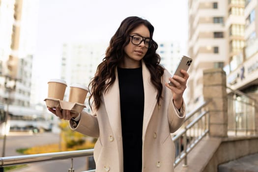 Business woman with cups of coffee looking at the phone.