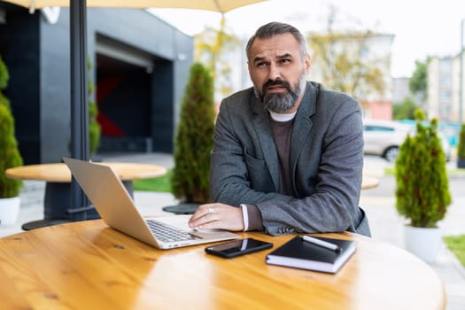 adult male businessman with beard working on laptop outside.
