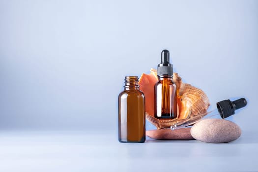 Two glass brown bottles with a pipette for a cosmetic product with a sea shell on stones. Natural cosmetics for face and body skin care. Selective focus. Place for text.