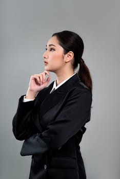 Confident young businesswoman stands on isolated background, posing in formal black suit. Office lady or manager with smart and professional appearance. Enthusiastic