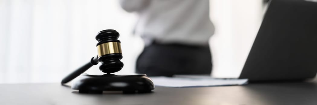 Focus wooden gavel hammer on blur background of lawyer working with legal document on desk at law firm office. Lawful hammer for righteous and equality judgment by lawmaker and attorney. Equilibrium