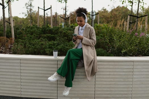 stylish african american girl student listening to music in headphones with a mobile phone in her hands outside.