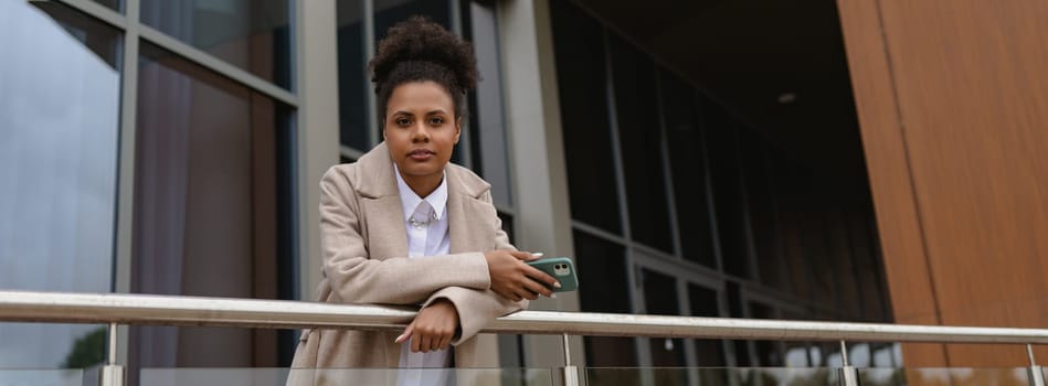 serious business african american woman in business clothes on the background of an office building looks at the camera.