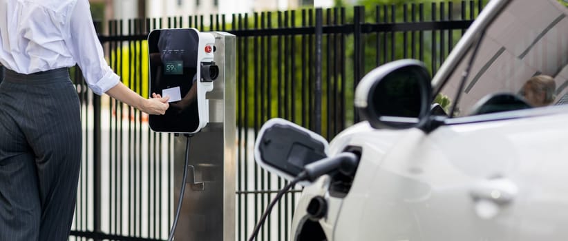 Credit card payment for eco-friendly clean and sustainable energy for electric vehicle at charging station. Progressive woman pay for charging point to power his electric rechargeable vehicle.