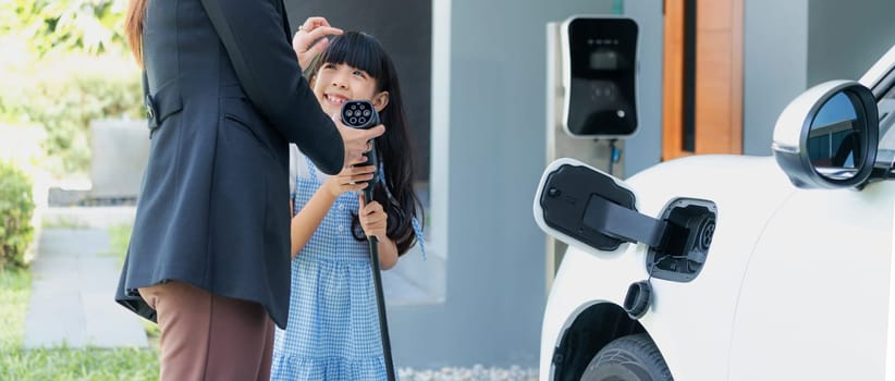 Progressive lifestyle of mother and daughter who have just returned from school in an electric vehicle that is being charged at home. Electric vehicle powered by sustainable clean energy.