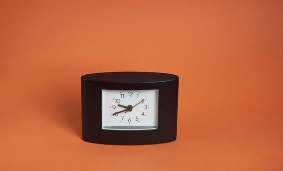 A square-shaped black desk clock with a white dial on a brown background and a place to copy text.