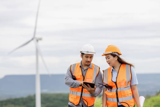 Male and female engineers working on a wind farm atop a hill or mountain in the rural. Progressive ideal for the future production of renewable, sustainable energy.