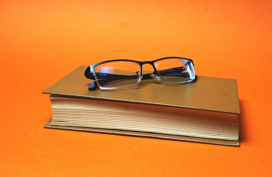 The glasses are on a brown book on a bright orange background