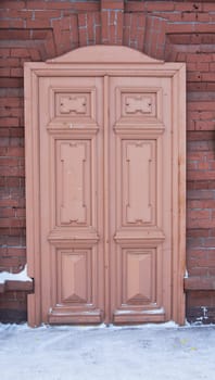 An old brown double-leaf wooden door on a brick wall