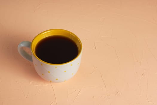 A white and yellow cup with black coffee on a light pink background.