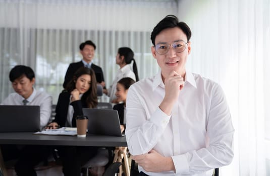 Portrait of focus young successful confident male manager, executive wearing business wear in harmony office arm crossed with blurred meeting background of colleagues, office worker.