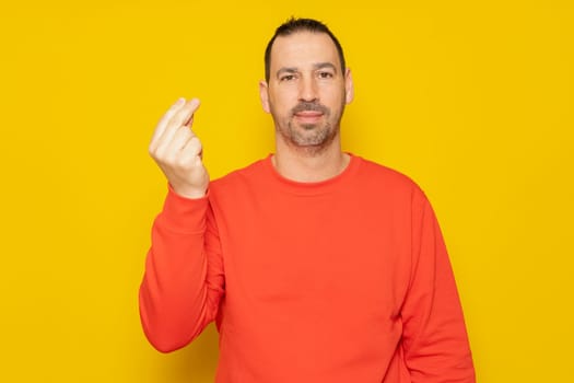 Bearded hispanic man wearing a red sweater in funny attitude making the italian gesture, isolated over yellow background