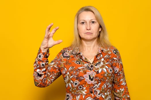 Caucasian blonde female with raised hand in the form of a claw ready to attack her prey, she is angry and dangerous. Isolated on yellow background