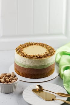 Pistachio cake on the table with cutlery and textiles. Ingredients: pistachio sponge cake, pistachio mousse, chocolate mousse and white chocolate mousse.