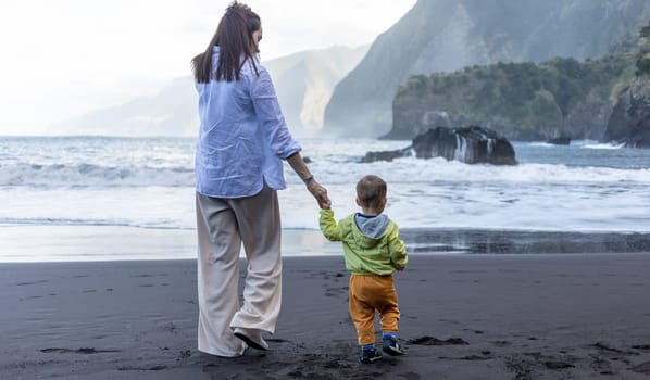 Mother and little child holding hands walking at sea side. High quality photo