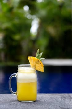 Fresh pineapple juice on swimming pool ledge on tropical paradise vacation resort. Copy space. No people. Vertical image. Vacation lifestyle concept.