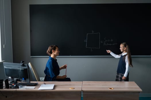 Caucasian little girl answers the question of the female teacher at the blackboard