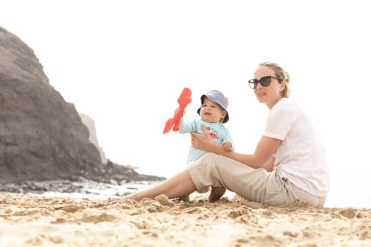 Mother playing his infant baby boy son on sandy beach enjoying summer vacationson on Lanzarote island, Spain. Family travel and vacations concept