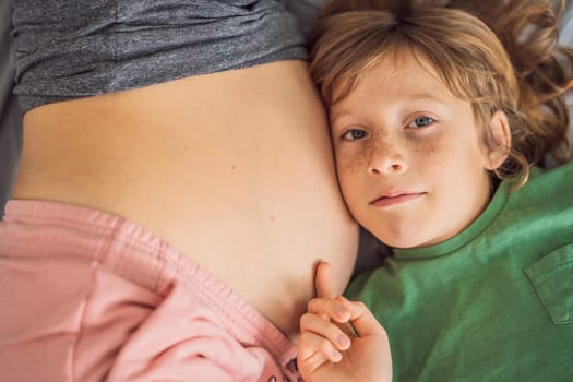 Young beautiful pregnant woman and eldest son. The cute boy leaned his ear against his mother's belly. Expecting a baby in the family concept. Preparing an older child for a younger one.