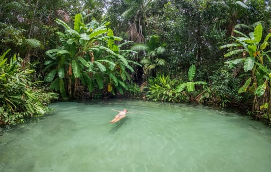 Unrecognizable woman floating on her back in a peaceful and isolated fervedouro in Jalapao, surrounded by lush green rainforest. Perfect for travel ads and vacation brochures.