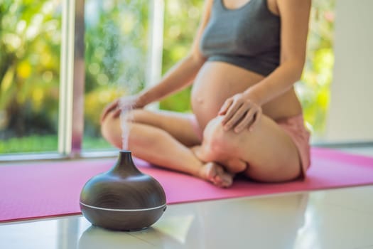Young pregnant woman doing yoga exercises and meditating at home with an aroma diffuser. Health care, mindfulness, relaxation and wellness concept. Aromatherapy during pregnancy.