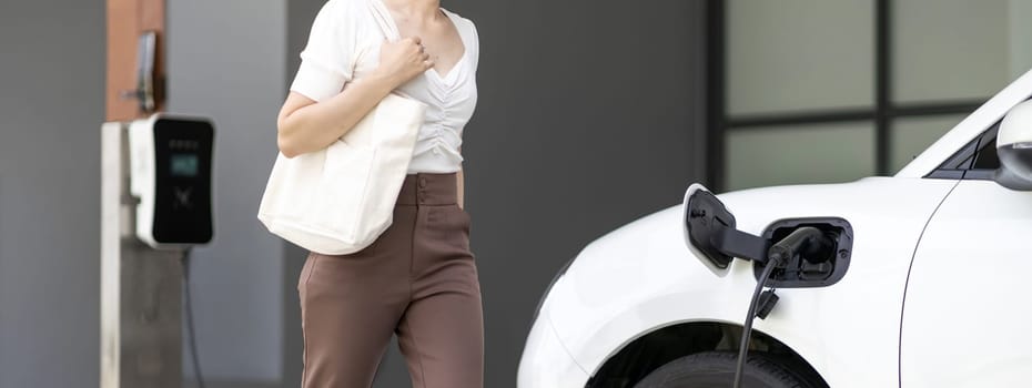 Progressive asian woman and electric car with home charging station. Concept of the use of electric vehicles in a progressive lifestyle contributes to a clean and healthy environment.