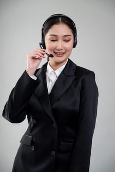 Attractive asian female call center operator with happy smile face advertises job opportunity on empty space, wearing a formal suit and headset on customizable isolated background. Enthusiastic