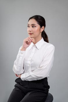 Confident young businesswoman sitting on a chair on isolated background, posing in formal black suit. Successful office lady or manager with smart and professional appearance. Enthusiastic