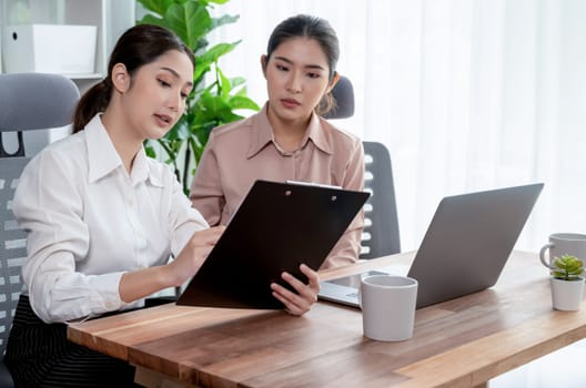 Two young office lady colleagues collaborating in modern office workspace, engaging in discussion and working together on laptop, showcasing their professionalism as modern office worker. Enthusiastic