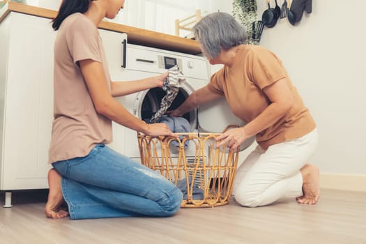 Daughter and mother working together to complete their household chores near the washing machine in a happy and contented manner. Mother and daughter doing the usual tasks in the house.