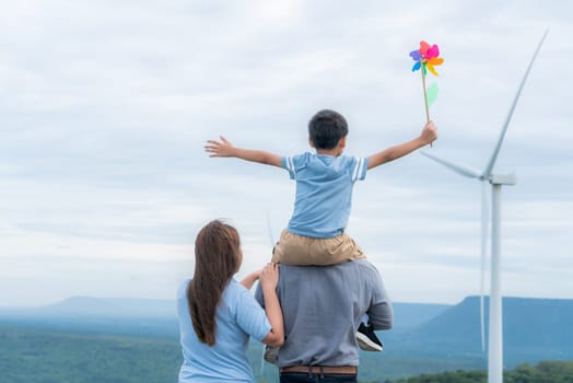 Progressive happy family enjoying their time at wind farm for green energy production concept. Wind turbine generators provide clean renewable energy for eco-friendly purposes.