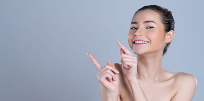 Glamorous beautiful woman with perfect makeup clean skin pointing finger in copyspace isolated background. Promotion indicated by hand gesture concept for skincare product advertisement.