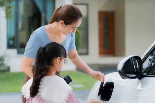 Progressive lifestyle of mother and daughter who have just returned from school in an electric vehicle that is being charged at home. Electric vehicle powered by sustainable clean energy.