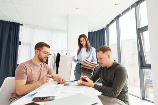 Cloth and fashion business. Three people works in the office by sitting by the table.