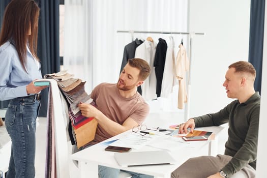 Cloth and fashion business. Three people works in the office by sitting by the table.