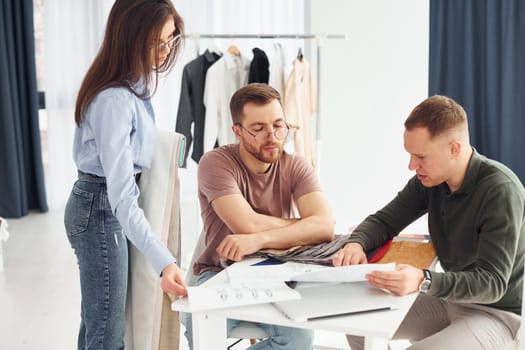 Cloth and fashion business. Three people works in the office by sitting by the table.