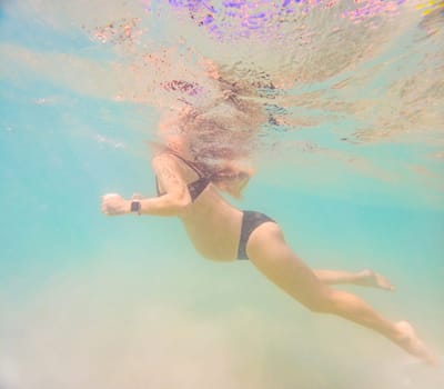 Pregnant woman underwater swimming in tropical sea. Healthy and active pregnancy. Young expecting mom on summer beach vacation before baby birth. Swim holiday and water fun. Travel during pregnancy. Underwater photography.