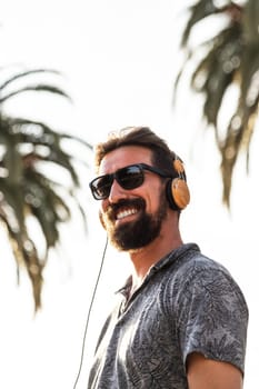 Vertical portrait of happy caucasian man with sunglasses listening to music outdoors looking at camera. Lifestyle.