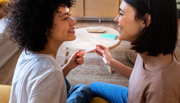 Multiracial lesbian couple in love, looking in the eyes, after finding out positive pregnancy test. LGBTQ love and family concept.