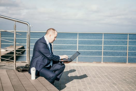 Digital Nomad, a young tattooed man working remotely online, typing on a laptop keyboard while sitting on a beach at sunset. Working remotely on vacation, running an online business from a distance