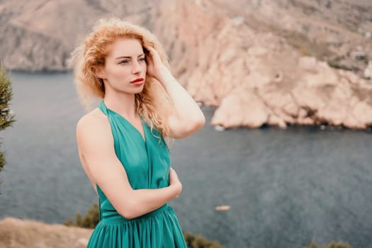 Side view a Young beautiful sensual woman in a mint long dress posing on a volcanic rock high above the sea during sunset. Girl on the nature on overcast sky background. Fashion photo