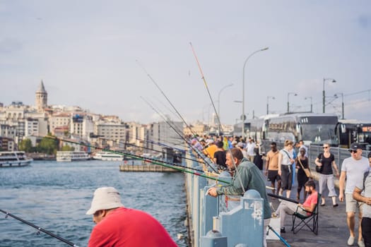Istanbul, Turkey - August 13, 2022: Local citizens fishing at golden horn on Galata Bridge before sunset with Galata Tower in the background, Eminonu district, Istanbul, Turkey.
