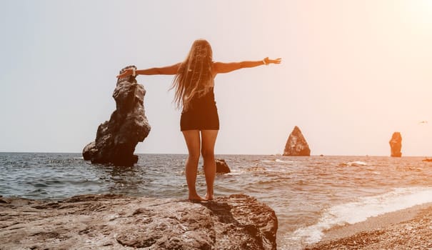 Woman travel sea. Young Happy woman in a long red dress posing on a beach near the sea on background of volcanic rocks, like in Iceland, sharing travel adventure journey